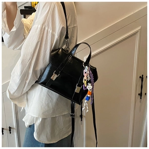 Detail of black glossy bucket backpack with silver buckle and colorful beaded pendant
