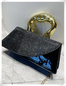 Close-up of black patent leather bag featuring a heart-shaped gold metal handle and sequins