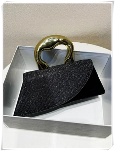 Detail of black sequined handbag featuring a unique gold wavy metal handle in a gift box