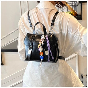 Detail of a shiny black mini backpack featuring a colorful woven rope and beaded charm