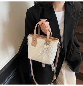 Detail der Mini-Beuteltasche in Creme und Braun mit Spitzenschleife und Perlenanhänger