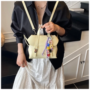 Detail of a beige bucket bag with decorative colorful beaded tassel held on a staircase