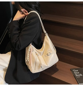 Detail of a beige soft leather tote bag with functional pockets and tassel on stairs
