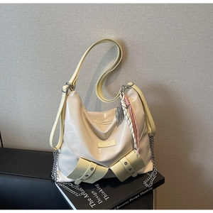Détail du sac cabas en cuir crème avec chaîne argentée et boucle latérale sur fond sombre