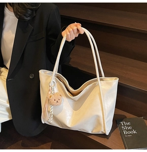 Detail of a creamy white tote bag with a plush bear charm on a dark wooden background