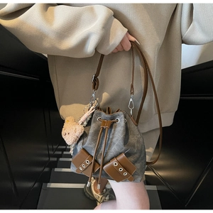 Detail der grauen Denim-Beuteltasche mit braunem Lederzug und Plüschbär-Anhänger