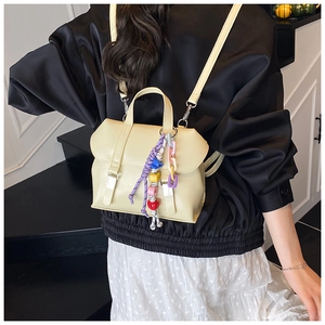 Detail of beige faux leather backpack featuring colorful braided charms and beaded chains