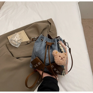 Detail der Retro-Jeans-Beuteltasche mit braunem Lederzugband und süßem Plüschbär-Anhänger