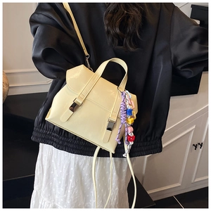 Detail of a cream bucket bag with metal buckles and a colorful beaded tassel charm
