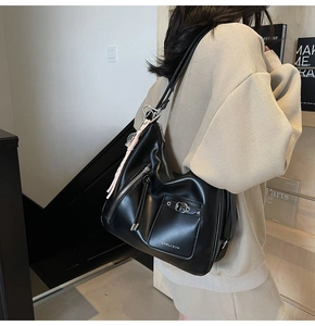 Close-up of black leather tote bag featuring a decorative pink tassel and metal buckle