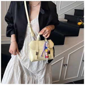 Detail of a creamy yellow bucket bag featuring a colorful beaded doll charm and metal buckles