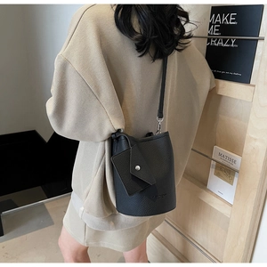 Detail of black lychee grain bucket bag with coin purse on stylish beige knit outfit
