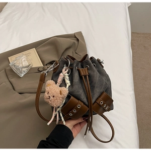 Detail der grauen Segeltuch-Beuteltasche mit Lederbesatz und süßem Plüschbären-Anhänger