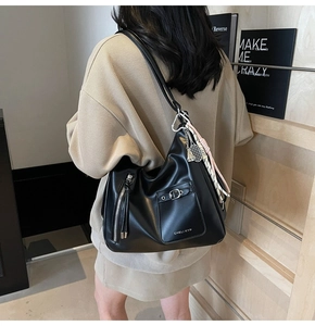 Detail of black leather tote bag featuring side zipper pocket and metal buckle decor