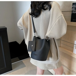 Detail of black lychee-textured bucket bag with crossbody strap and matching small pouch