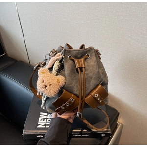 Detail der grauen Canvas-Beuteltasche mit braunem Leder und süßem Plüschbären-Anhänger
