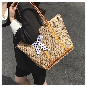 Detail of straw tote bag with orange handles and black white polka dot ribbon bow