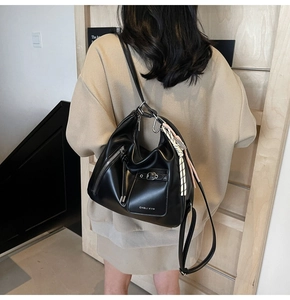 Detail view of large black leather tote bag with buckle pocket and braided rope charm