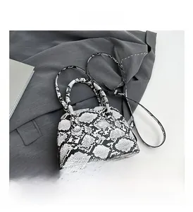 Detailsicht der monochromen Schlangenhaut-Muscheltasche auf dunklem Blazer mit Trageriemen