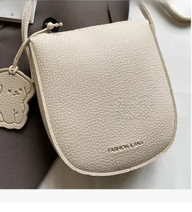 Gros plan d'un sac bandoulière en cuir blanc cassé avec pendentif chien et logo gravé