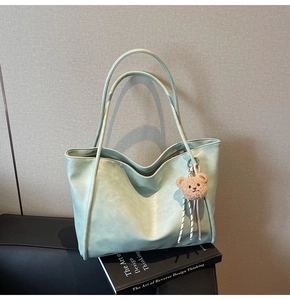 Detail of light green tote bag with bear charm on English books over a black chair