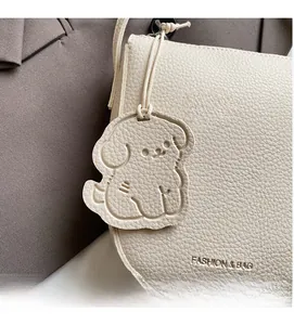 Détail du sac seau en cuir blanc crème à motif litchi avec un charmant pendentif chien