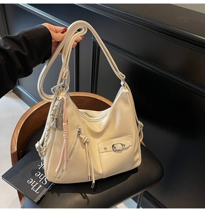 Detail of cream hobo bag showing multiple thin straps and metallic racket pendant