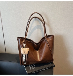 Detail view of large dark brown tote bag with smooth texture and cute bear pendant
