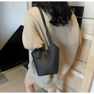 Detail view showing a black lychee pattern leather bucket bag worn as a shoulder bag