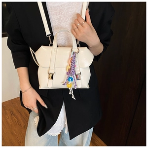 Detail of a creamy white leather handbag with multi-colored woven rope charm and dual buckles