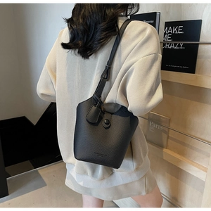 Close-up of a minimalist black lychee grain leather bucket bag with adjustable strap