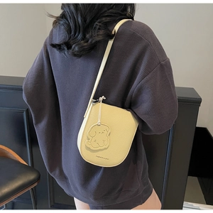 Détail d'un sac besace en cuir jaune pâle avec breloque chien porté par un mannequin