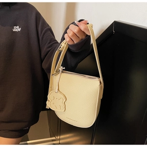 Détail du sac selle crème avec breloque chien en cuir et texte gaufré