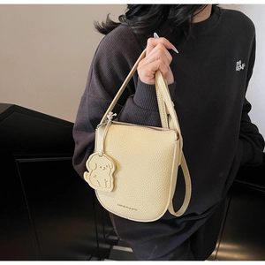 Détail d'un sac selle jaune crème avec texture litchi et breloque chiot mignonne