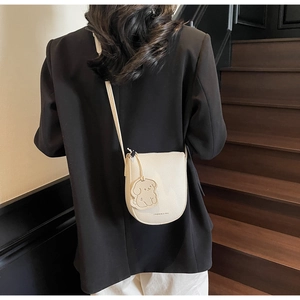 Mini sac besace beige avec charm chiot porté par un mannequin sur un escalier