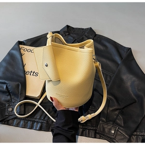 Detail view of yellow lychee leather bucket bag with a mini pouch and brand logo text