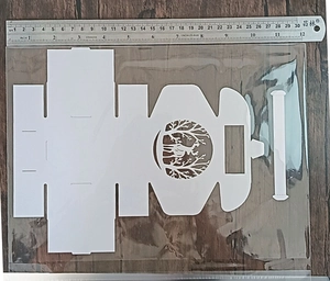 Flat laser-cut white cardstock box template with deer and tree design on wood background