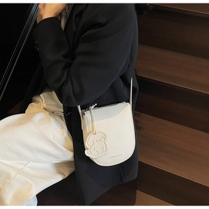 Détail d'un sac selle en cuir blanc avec breloque chien et logo fashion imprimé