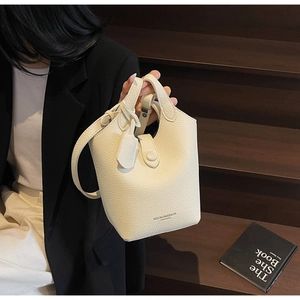 Detail of creamy white pebble leather bucket bag with cutout handle and shoulder strap