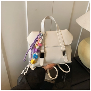 Close-up of white leather backpack featuring colorful beaded charm and metal buckle detail