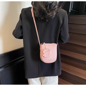 Détail du sac seau rose en cuir litchi avec breloque chiot porté par un mannequin