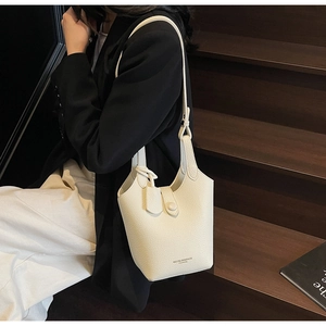 Detail of a white bucket bag with pebble leather texture worn by a model on stairs