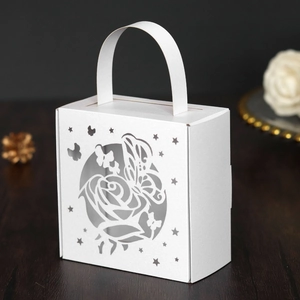 Close-up of white laser-cut wedding favor box with intricate rose and butterfly patterns