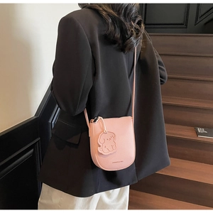 Sac selle rose avec breloque chien porté à l'épaule sur un fond urbain minimaliste