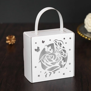 Close-up of laser-cut white wedding favor box with intricate rose and butterfly patterns