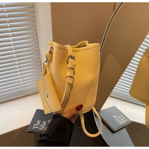 Close-up of yellow bucket bag featuring pebble leather texture and gold logo detail