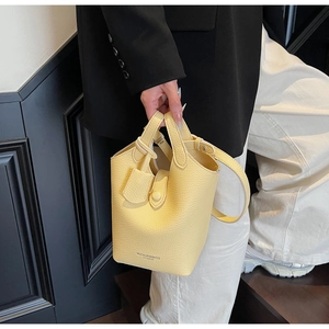 Detail of yellow lychee leather bucket bag with dual handles and logo print