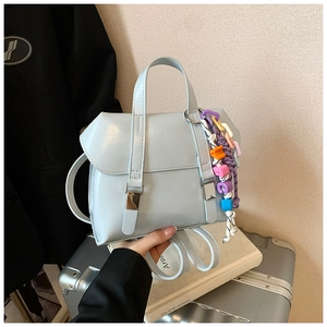 Detail of light blue glossy handbag with colorful decorative chain on silver suitcase