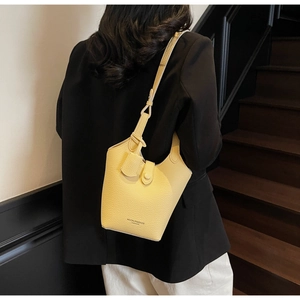 Detail of yellow lychee textured bucket bag worn by model in a modern staircase setting