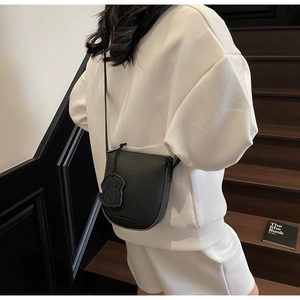 Détail du sac de selle noir en cuir grainé avec un charme de chiot sur un escalier en bois